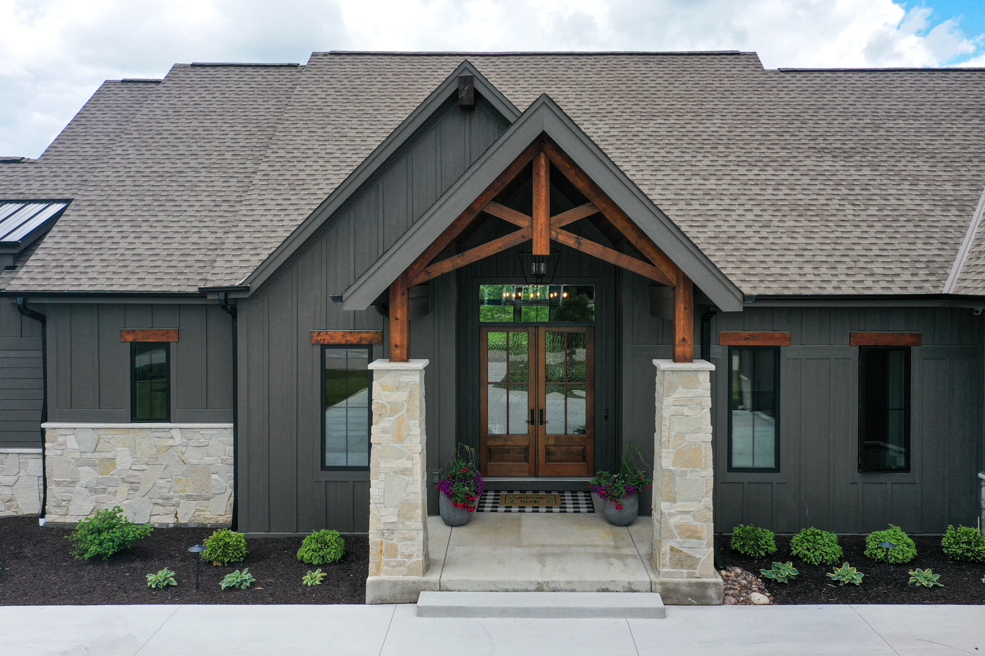 Front exterior of a custom-built Pewaukee home featuring stone pillars and wood accents, epitomizing custom home design in the area.