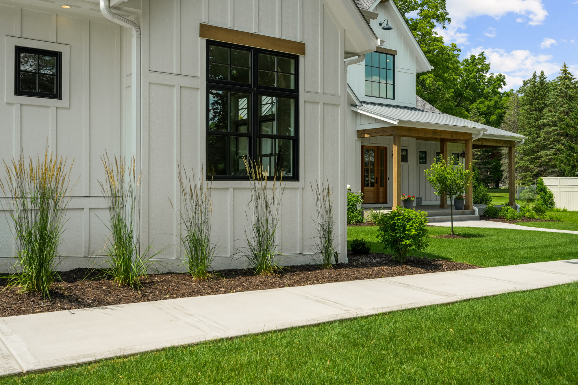 Charming white farmhouse-style exterior with board and batten siding and wood accents by Brookfield WI custom home builders.