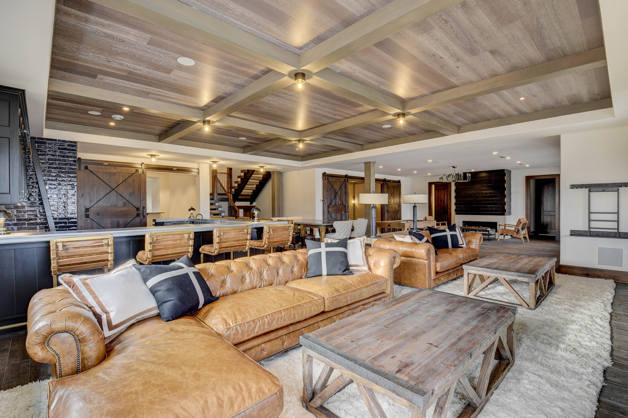Warm and inviting basement living area with wood coffered ceilings, leather seating, and farmhouse touches designed by country style home builders