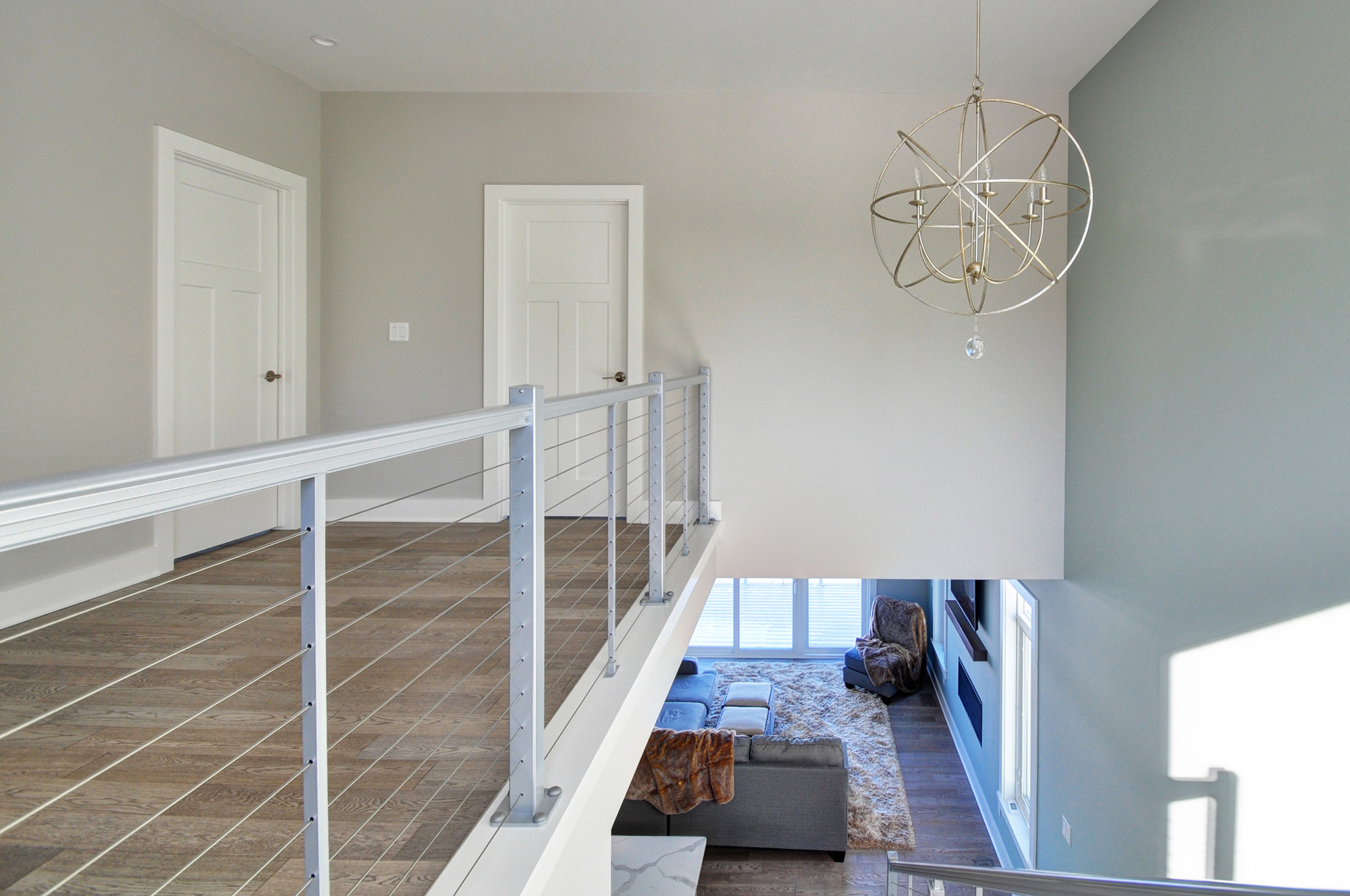 Second-floor hallway with modern cable railing and open view to the living room, showcasing clean lines and airy layout in a Wisconsin lake home design.